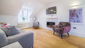 A modern living room with a high ceiling, a fireplace, a television, and a colorful chair. - Penthouse  apartment (Cumbria)