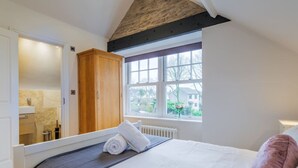 A bedroom with a bed, a window, a wooden wardrobe, and a bathroom visible through an open door. - Penthouse  apartment (Cumbria)