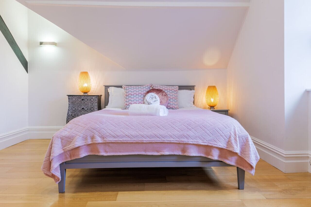 A bedroom with a bed, two bedside tables, and two wall-mounted lamps.