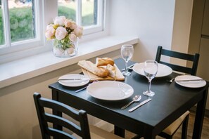 A dining table set with plates, cutlery, a wine glass, and a loaf of bread on a black table. - Oak View- Free access to local Health Club (Bowness-on-Windermere)