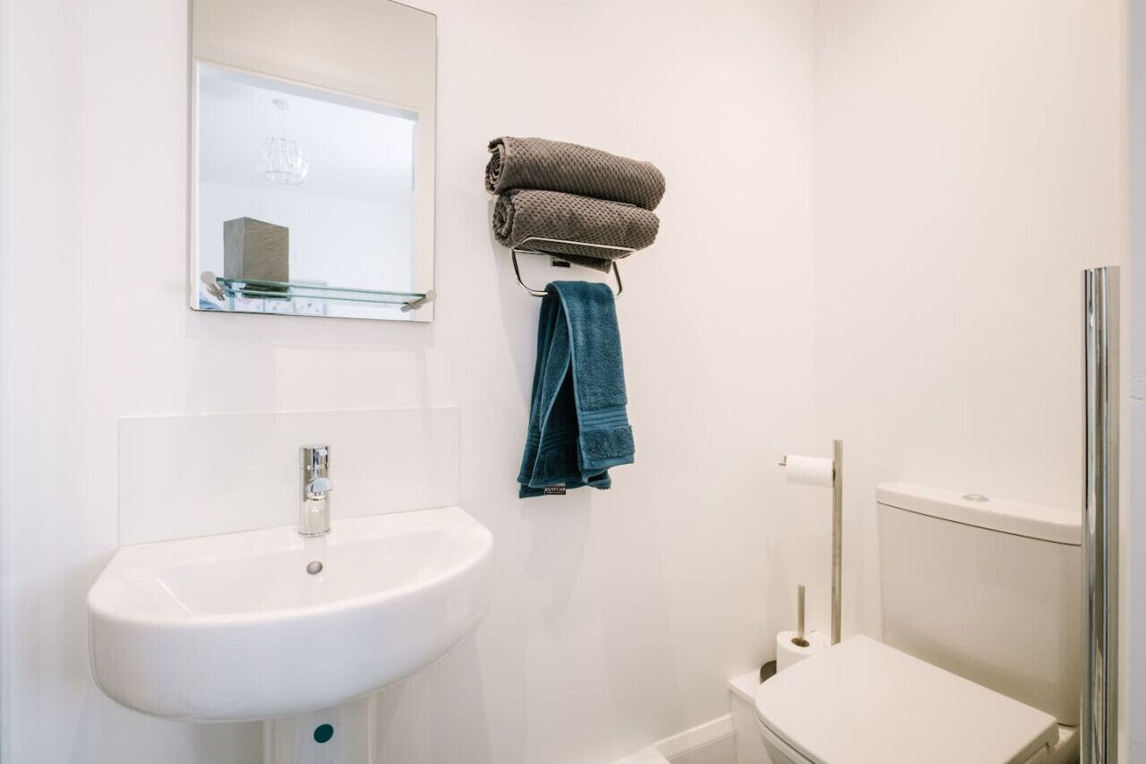A bathroom with a white sink, a mirror, a towel rack with towels, and a toilet.