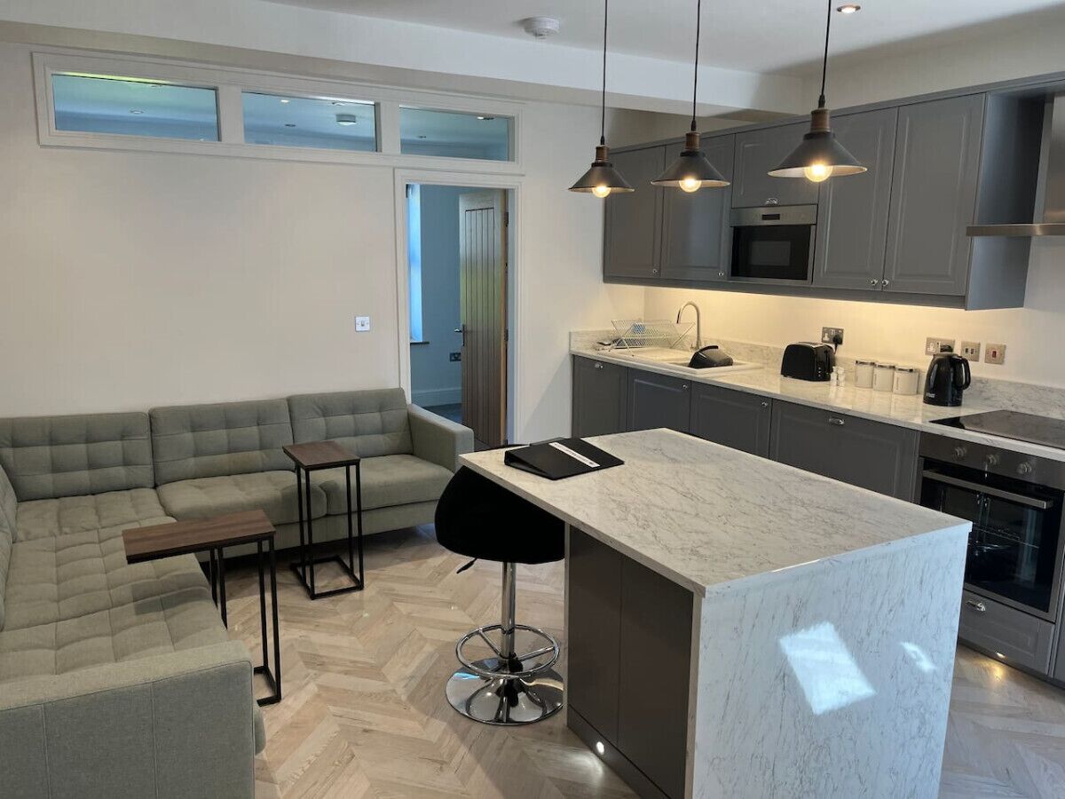 A modern kitchen with grey cabinets, a marble countertop, and pendant lighting.
