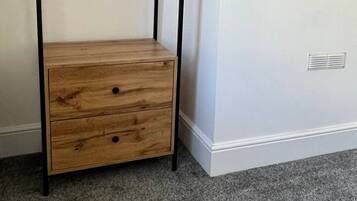 A room with a wooden bench with drawers, a round mirror on the wall, and a vent near the floor.