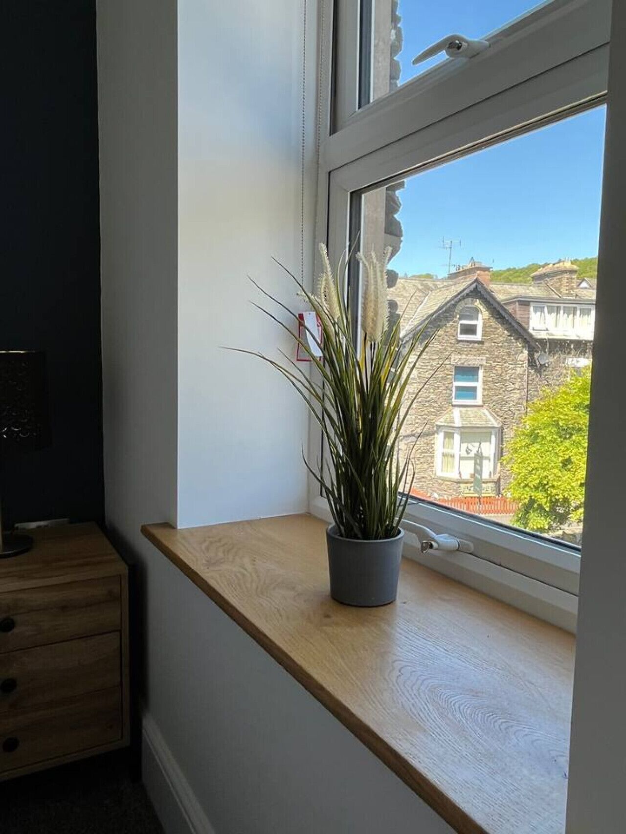 Finestra amb vista a un edifici de pedra i una planta sobre un prestatge de fusta.