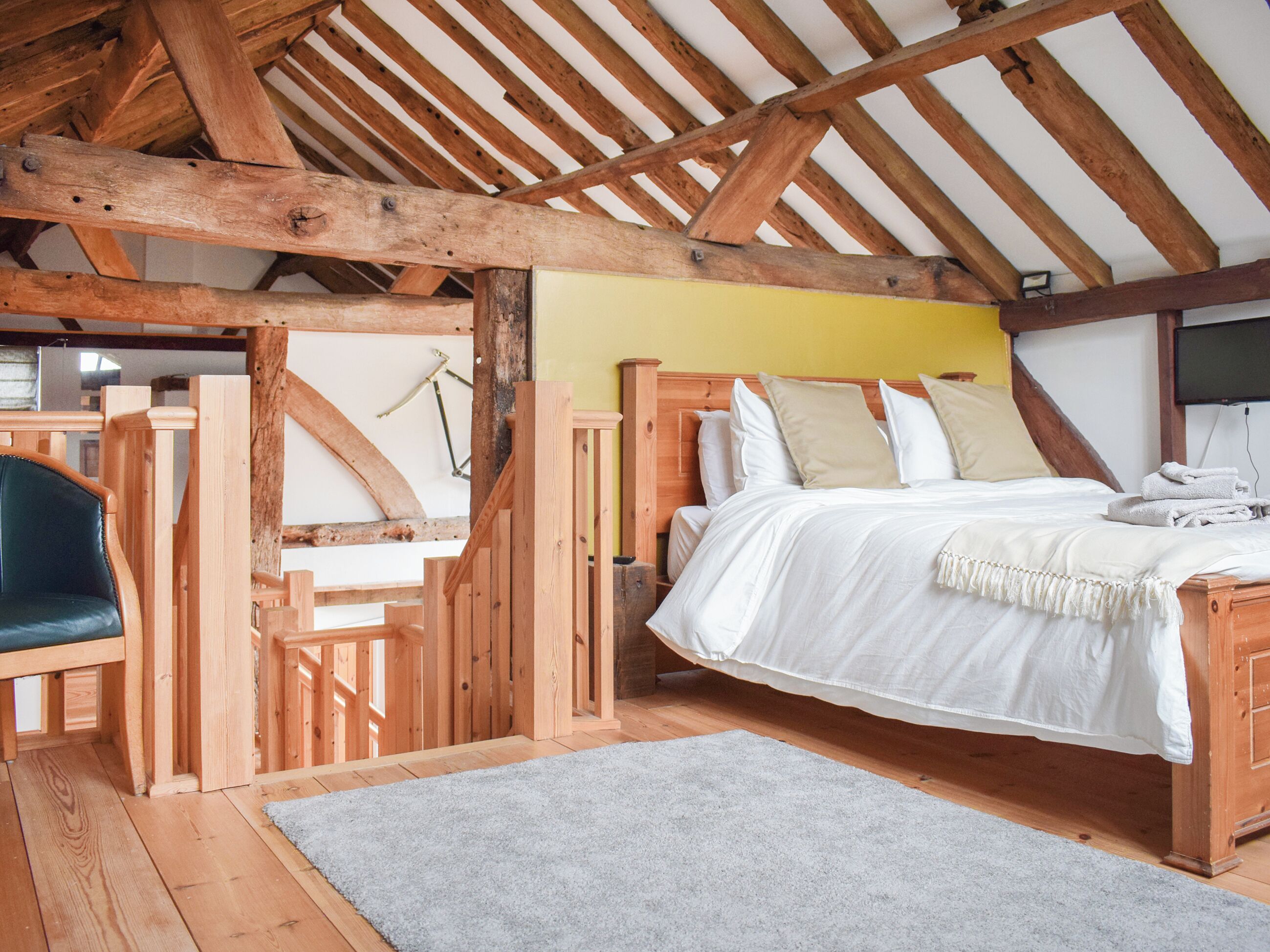 Un dormitorio con techo de madera, una cama con ropa de cama blanca, un tapete gris y una silla de madera.