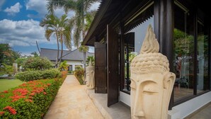 Un sendero conduce a una villa moderna con fachada de piedra, palmeras y un jardín cuidado.