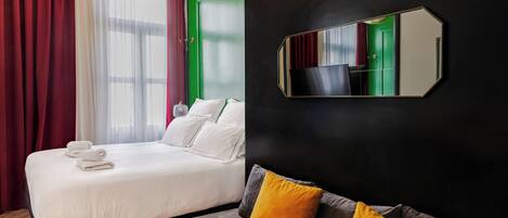 A hotel room with a bed, a sofa, a large mirror, and a window with curtains.