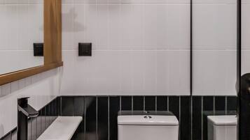 A modern bathroom with a white sink, black and white tiled walls, a toilet, and a mirror with a light fixture.