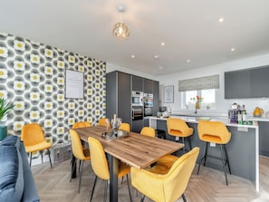 A modern kitchen with a built-in oven, a dining area with a wooden table and yellow chairs, and a patterned wall.