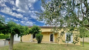 A yellow building with a tiled roof, a covered patio with chairs, and a well-maintained lawn. - Villa 6p, 3ch Avec Grand Jardin Arboré Clos, Clim, Village Classé de Vogue (Vogüé)