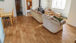 A spacious living room with a wooden floor, a sofa set, a dining table with chairs, and a large window providing natural light. - Sheemore View (Carrick-on-Shannon)