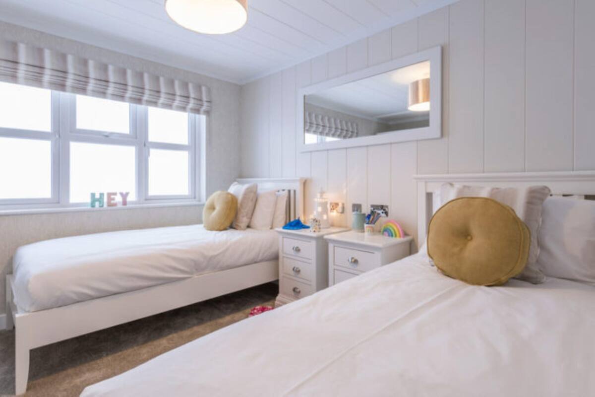 A hotel room with two single beds, a nightstand with a lamp, a mirror, and a window with curtains.