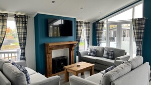 A modern living room with a fireplace, grey sofas, and a television. - Sure Studio by Best Western Brackenborough Lakes & Resort (Louth)