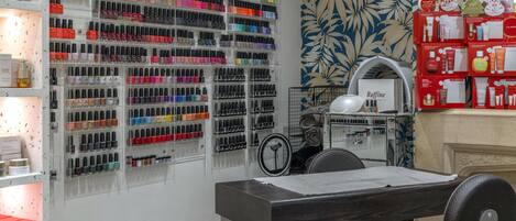 Un salón de manicura con varias estanterías llenas de esmaltes, un espejo y una silla.
