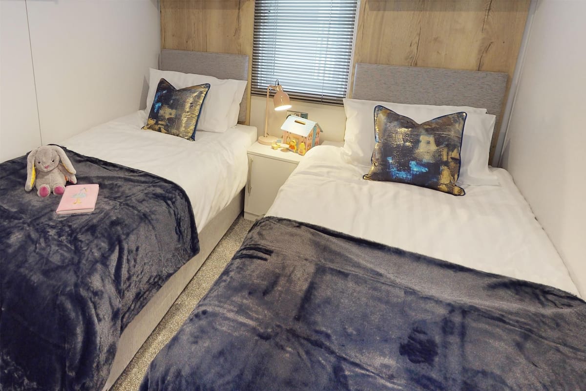 A twin room with two beds, each with a headboard, a bedside table with a lamp, and a small toy house.