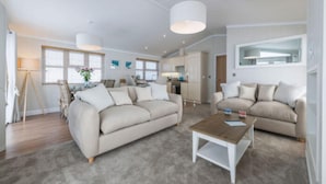 A spacious living room with two beige sofas, a wooden coffee table, and a large window. - Sure Studio by Best Western Brackenborough Lakes & Resort (Louth)