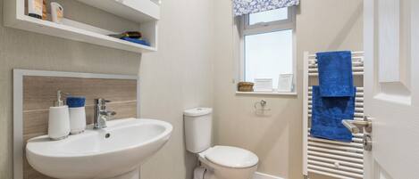 Un baño moderno con lavamanos, inodoro y toallero blancos.