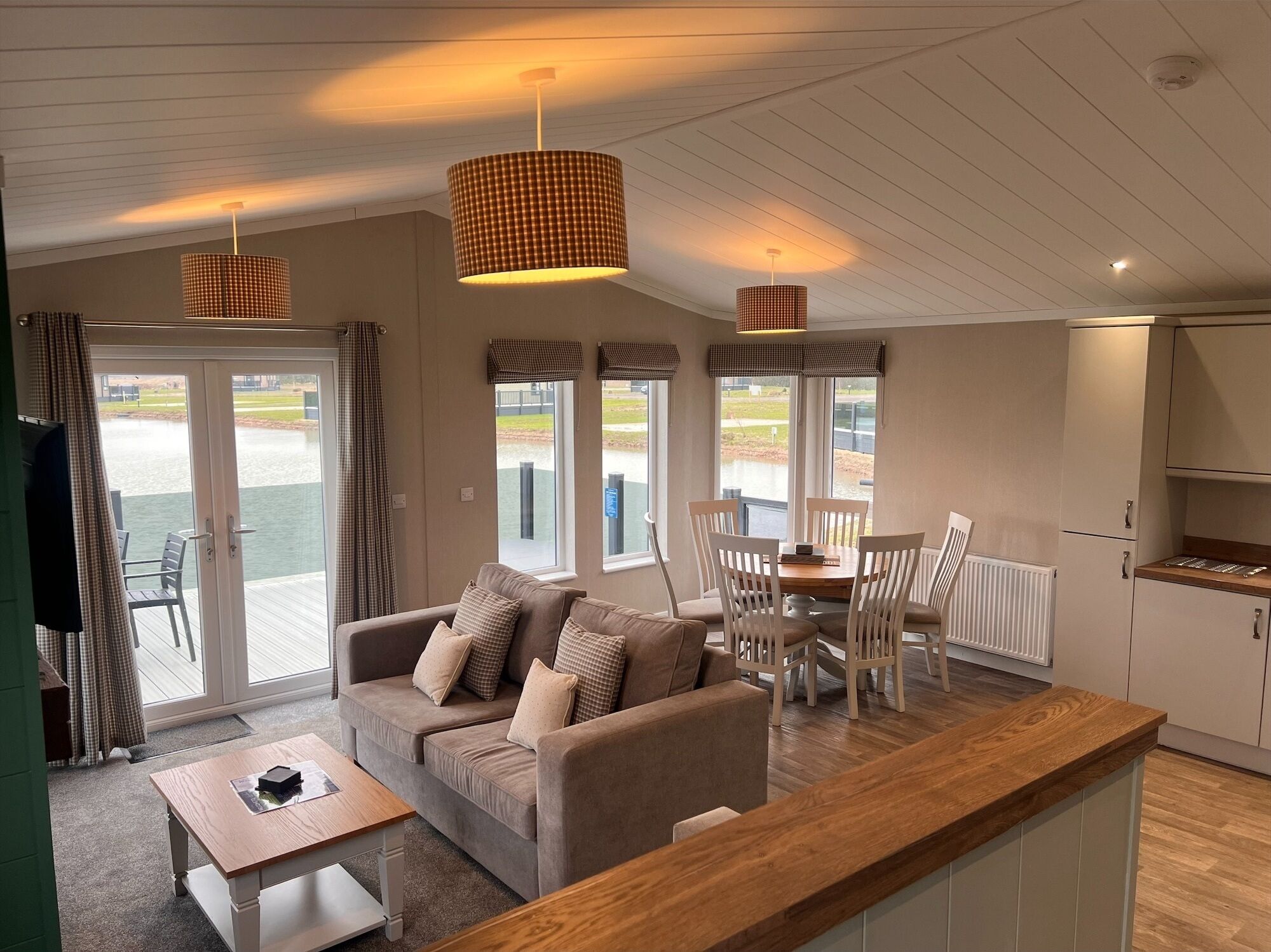 A cozy living area with a sofa, dining table, and chairs, a kitchen area with cabinets, and large windows offering a view of a body of water.
