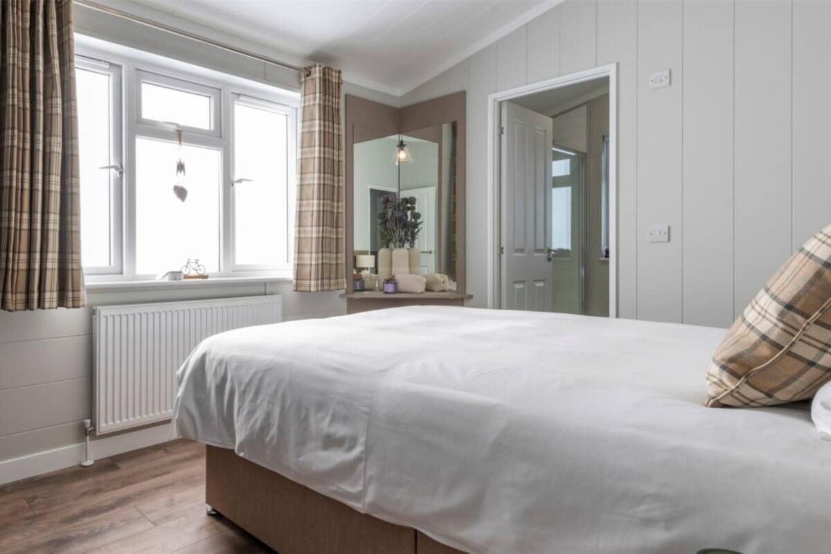 A bedroom with a bed, a radiator, a window with curtains, a mirror, and a plant.