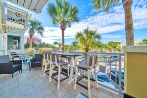 An outdoor patio with wicker furniture, a pool, and palm trees.