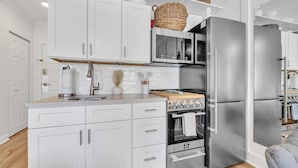 A modern kitchen with white cabinetry, stainless steel appliances, and a wooden countertop.