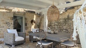 Un espace de restauration extérieur avec des murs en pierre, des meubles en osier et un luminaire suspendu.
