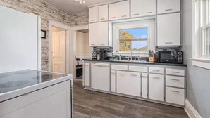 A modern kitchen with white cabinets, a built-in microwave, and a window with a view of the outdoors. - Renovated Victorian Home with Private Garden & Fire Pit! (Three Oaks)