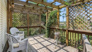 A wooden deck with lattice panels, wicker chairs, and a small table. - Renovated Victorian Home with Private Garden & Fire Pit! (Three Oaks)