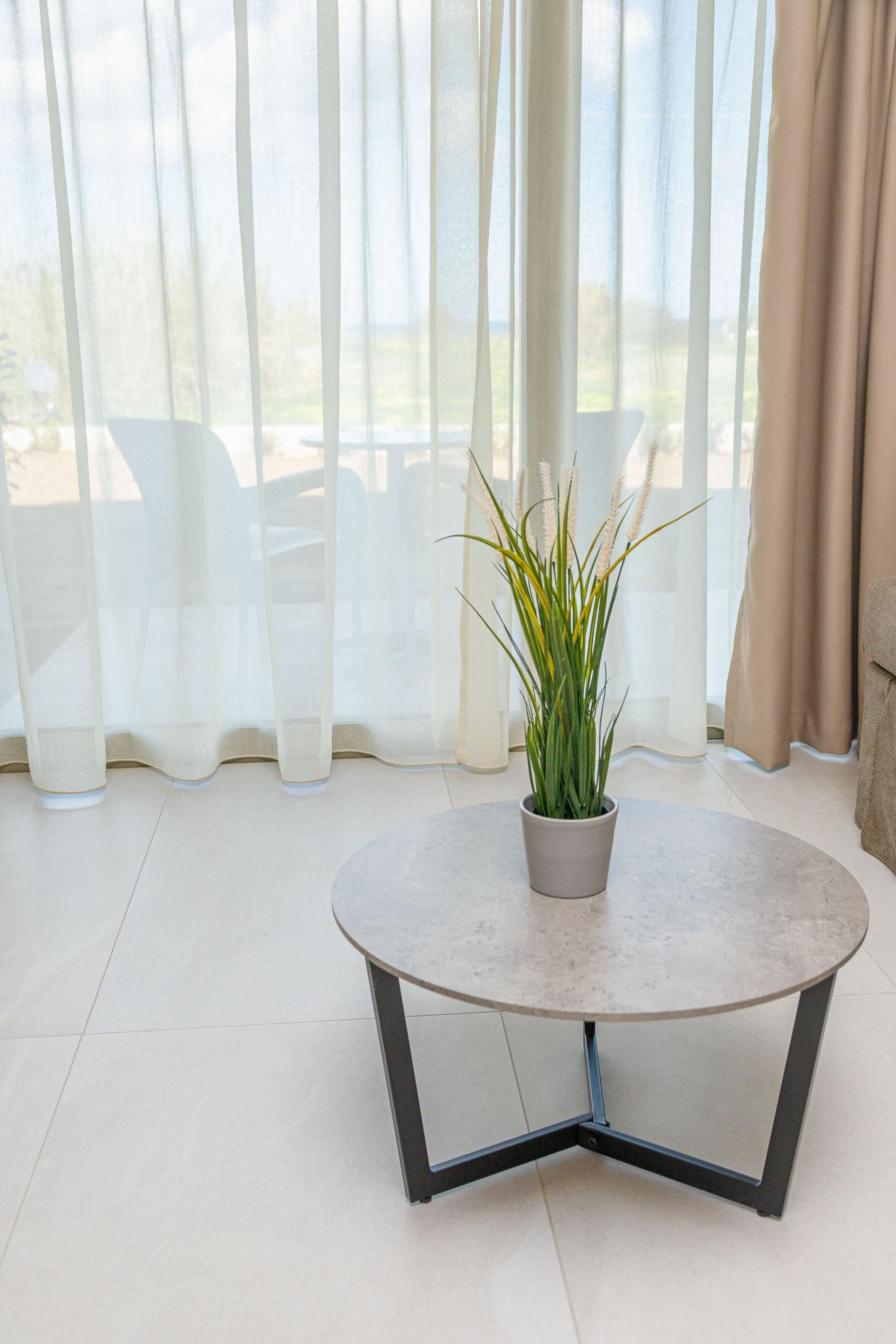 Een ronde tafel met een potplant in het midden, staand in een kamer met uitzicht door dunne gordijnen.