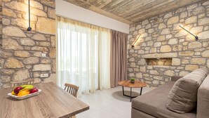 A room with a stone wall, a wooden table with fruit, a sofa, and a small round table. - Achatis Apartments with sea view (Platanias)