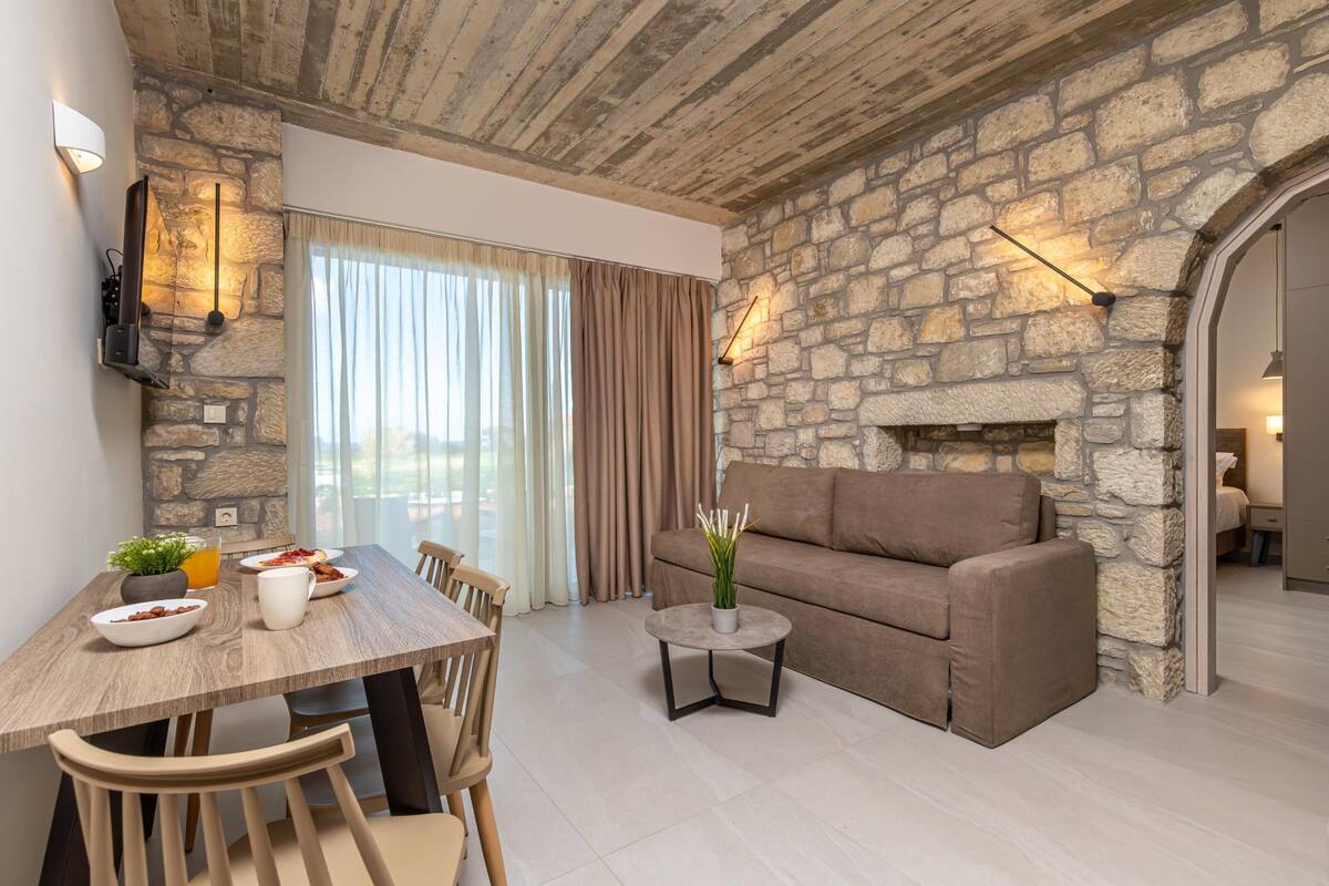 A modern living room with a stone wall, a fireplace, a sofa, and a dining area with a table and chairs.