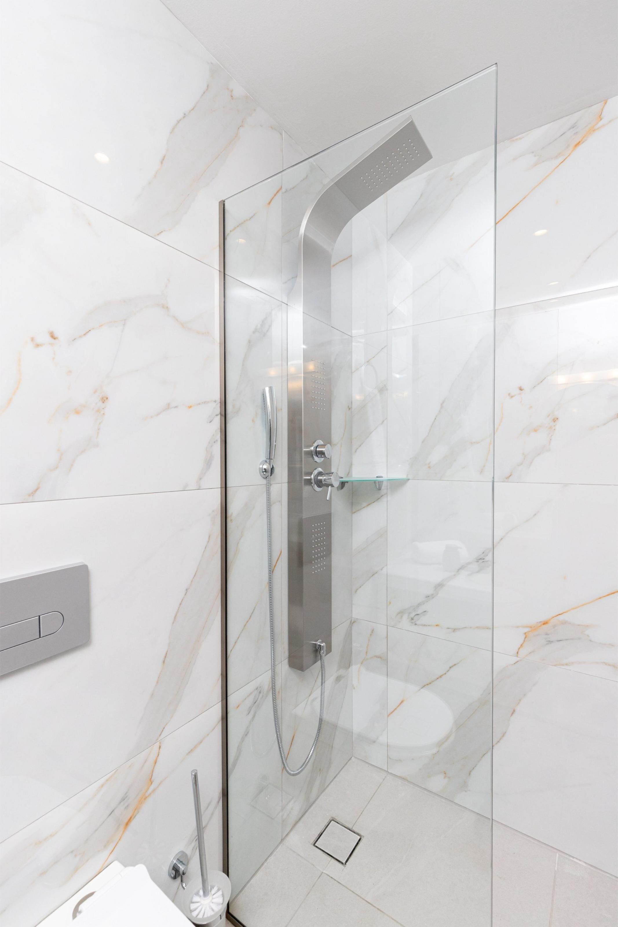Un baño moderno con ducha de vidrio, baldosas de mármol y un inodoro a la vista.