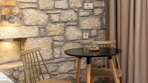 A room with a stone wall, a round table with two chairs, a bed, and a curtain. - Achatis Apartments with sea view (Platanias)