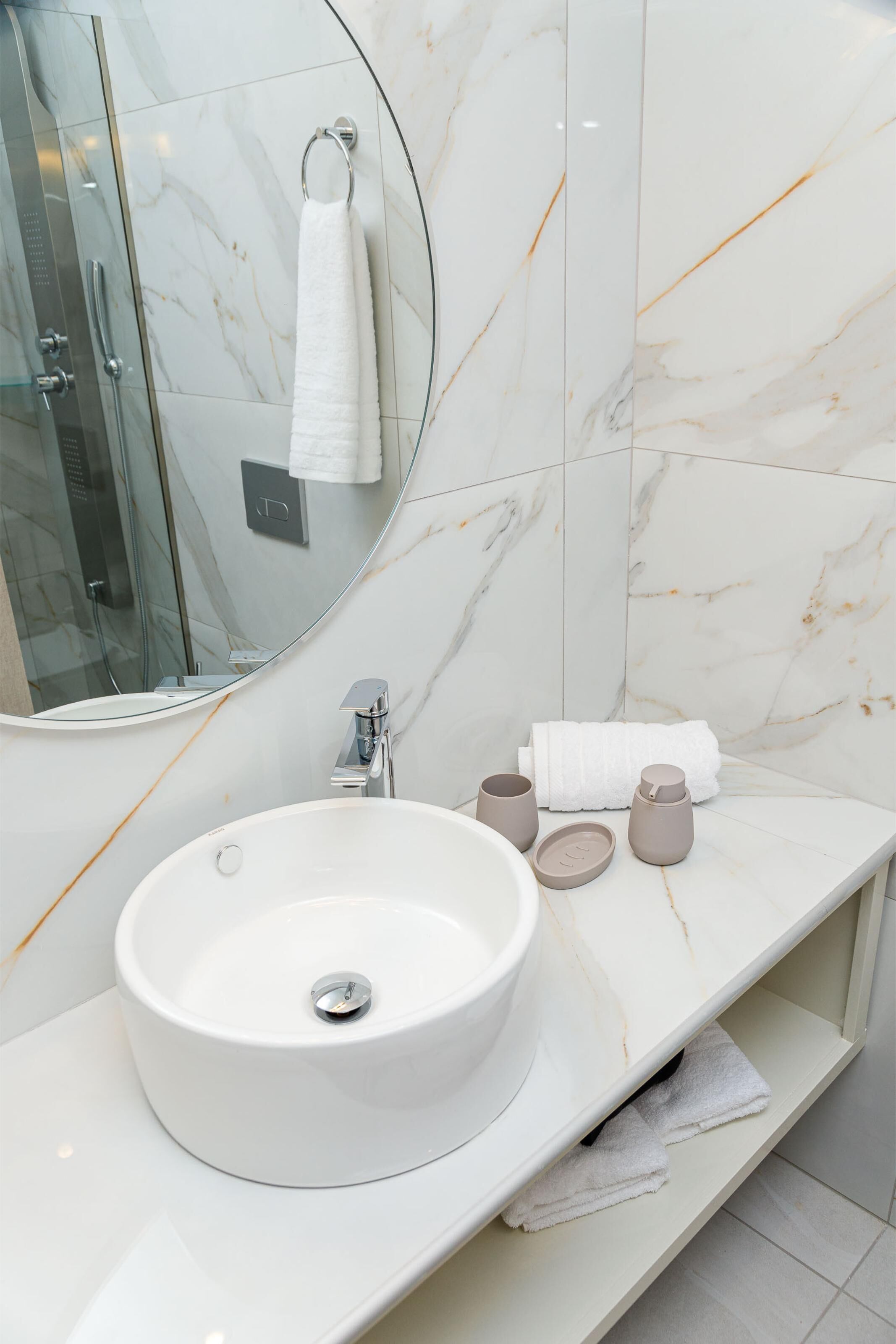 A bathroom with a white marble sink, a round mirror, and a glass shower enclosure.