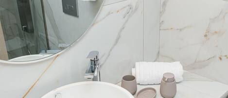 A bathroom with a white marble sink, a round mirror, and a glass shower enclosure.