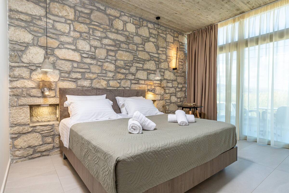 A bedroom with a stone wall, a bed with white linens, and two bedside lamps.