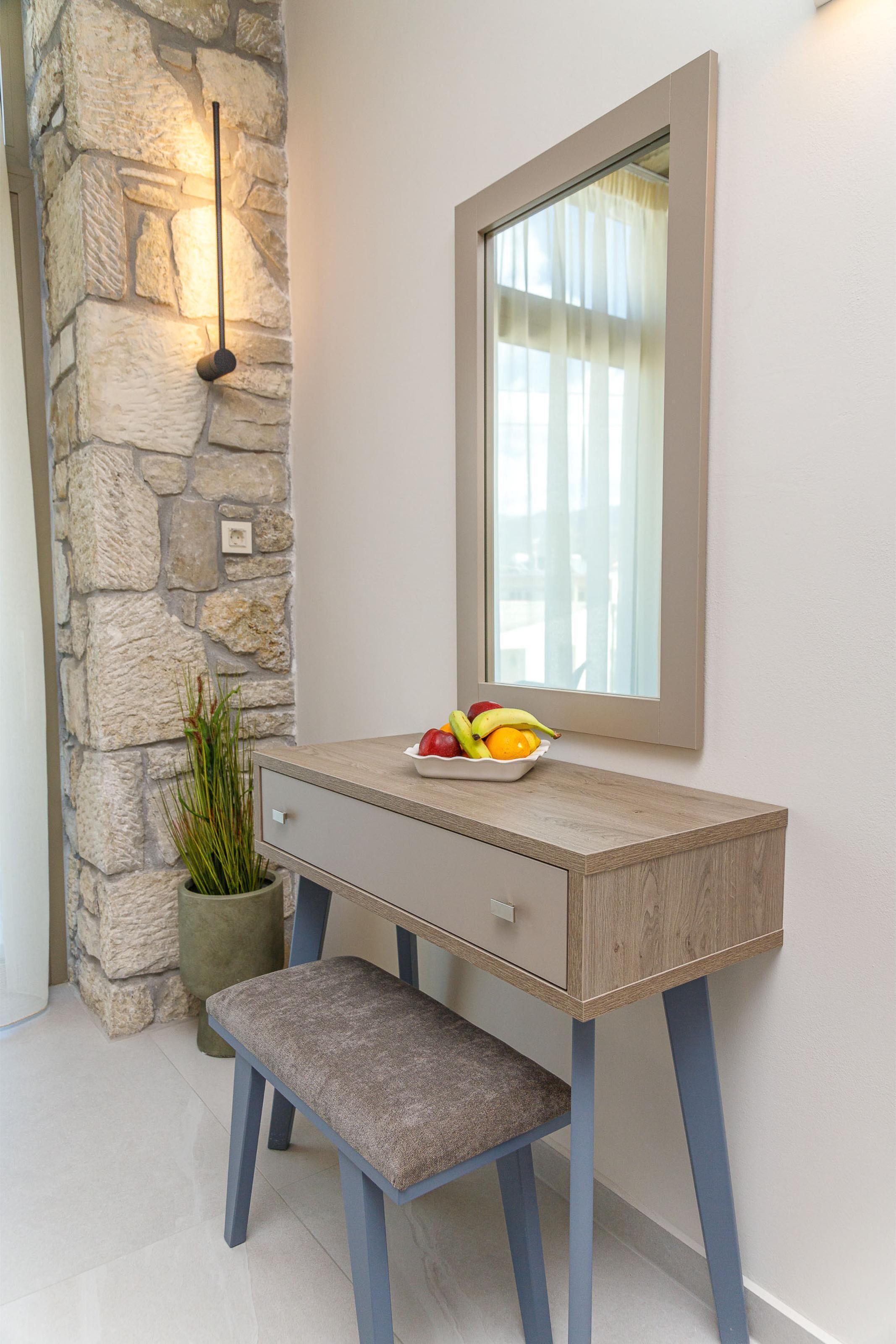 A wooden console desk with a mirror, a bowl of fruit, and a potted plant.