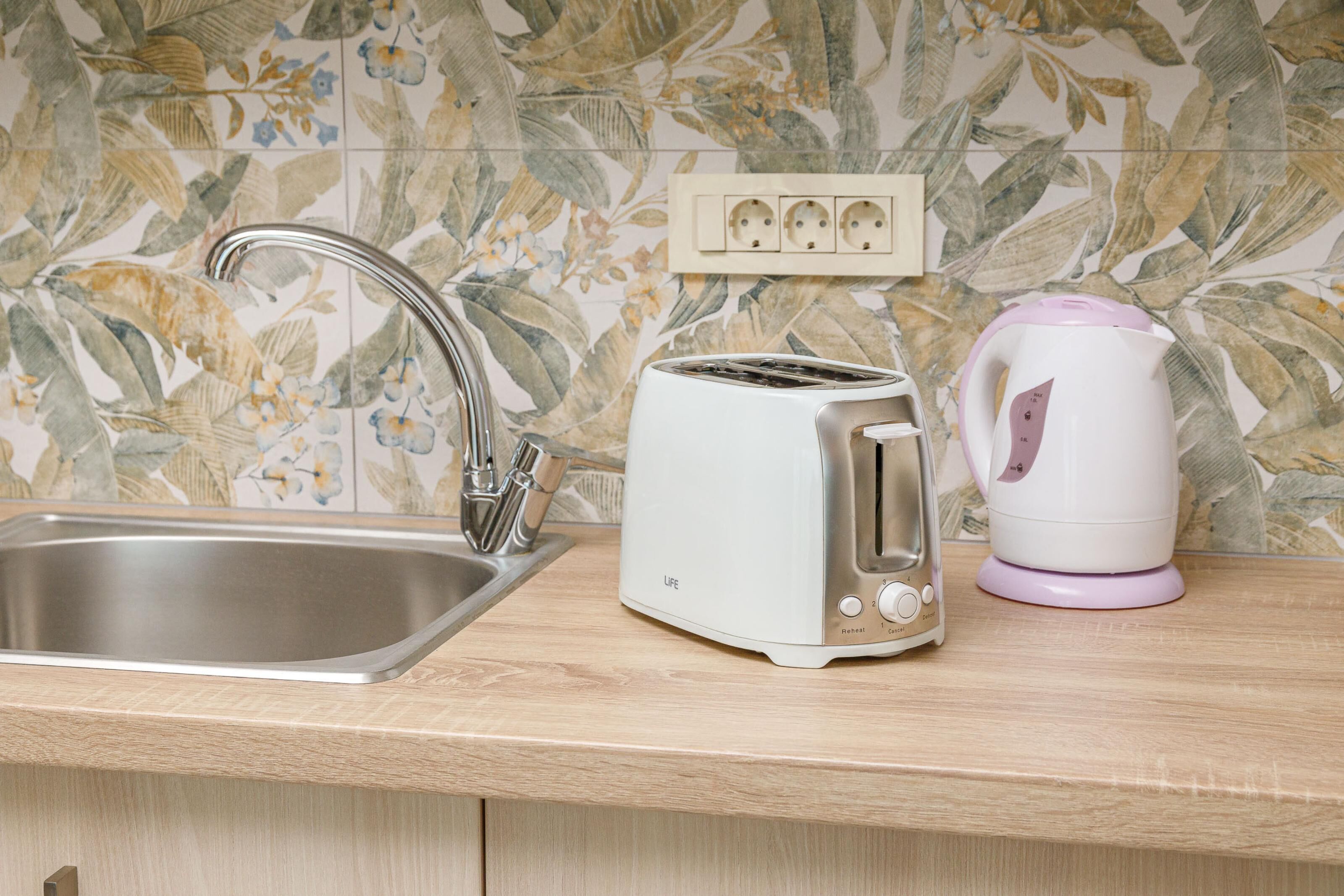 A kitchen with a stainless steel sink, a white toaster, and a white electric kettle on a wooden countertop.