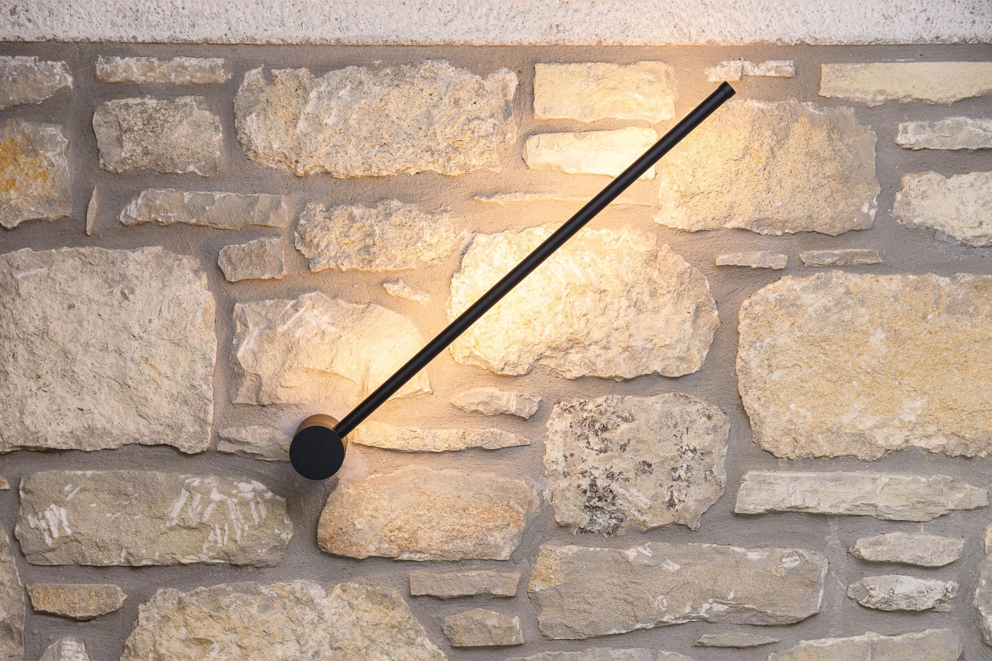 A stone wall with a black, modern light fixture.