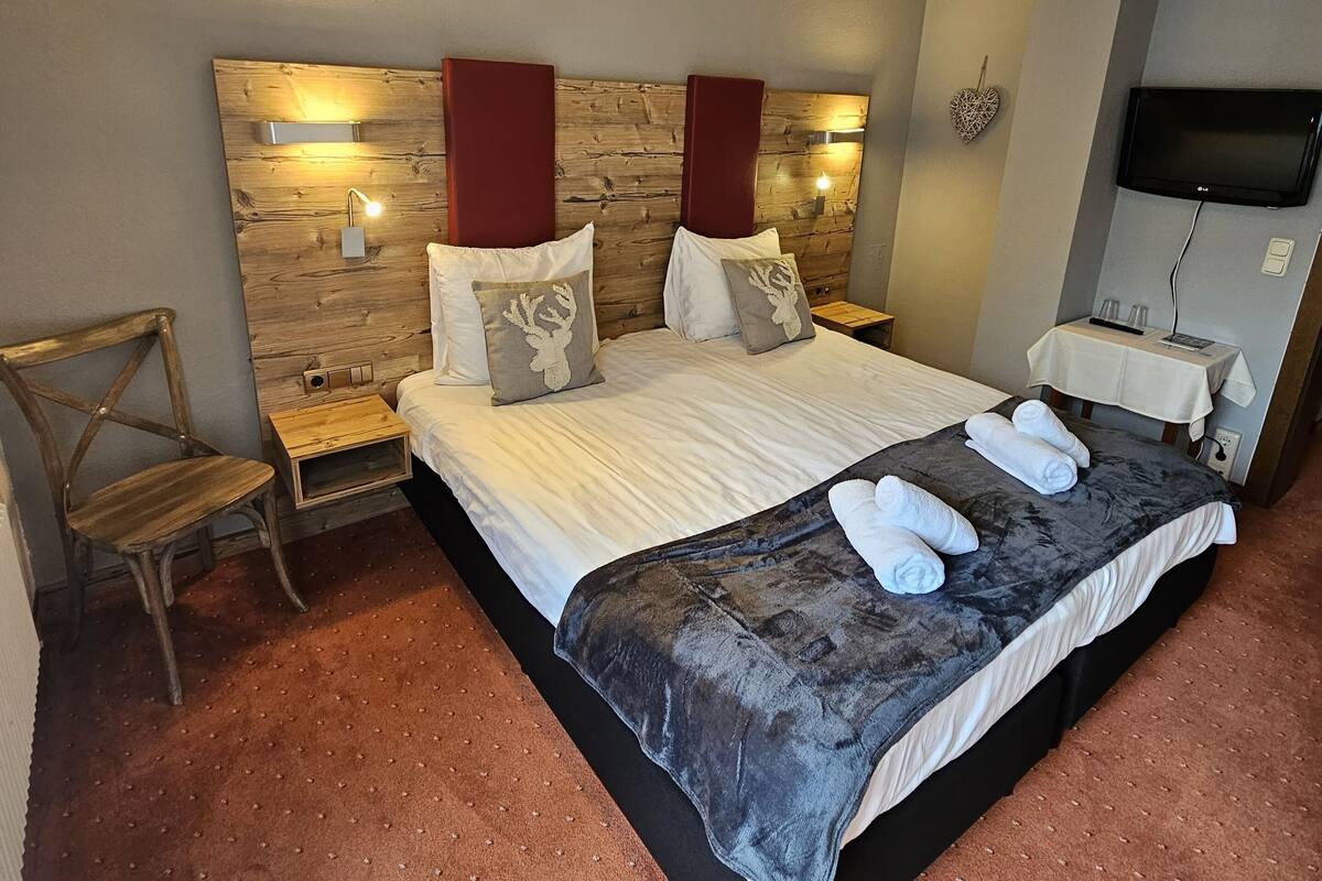 A hotel room with a large bed, a wooden headboard, a television, and a small table with a chair.