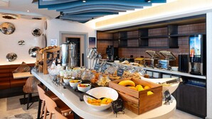 A breakfast bar with various food items, a coffee machine, and a seating area with chairs. - ibis Styles Burton Upon Trent - Hotel & Suites (Burton on Trent)