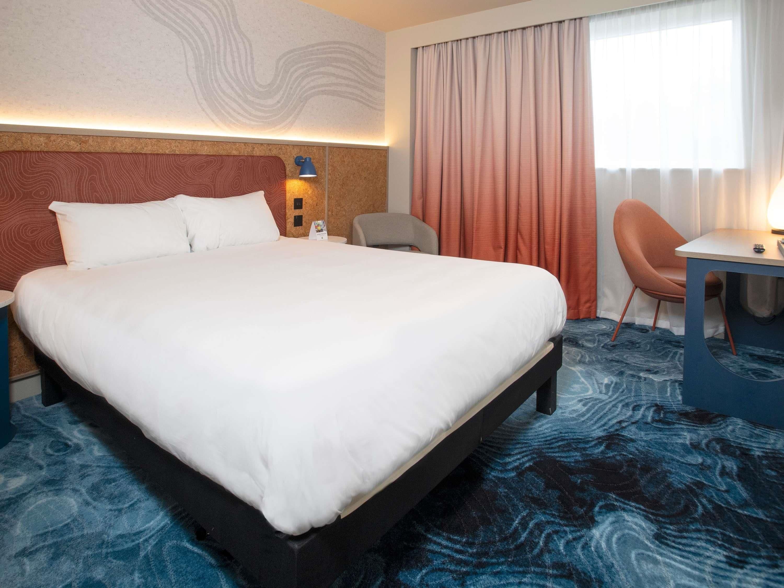 A hotel room with a large bed, a desk, a chair, and a view of the outdoors.