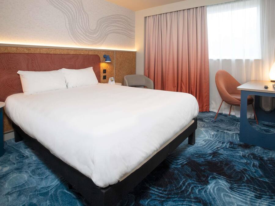 Habitación de hotel con una cama grande, un escritorio, una silla y vistas al exterior.