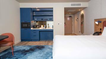 A hotel room with a bed, a desk, a chair, a kitchenette, and a bathroom.