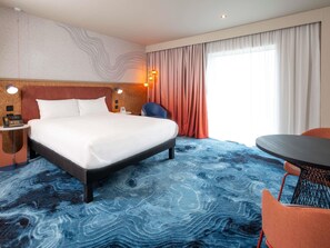 Habitación de hotel con una cama grande, un escritorio con teléfono, una silla, una mesa redonda y vistas al exterior a través de la ventana.
