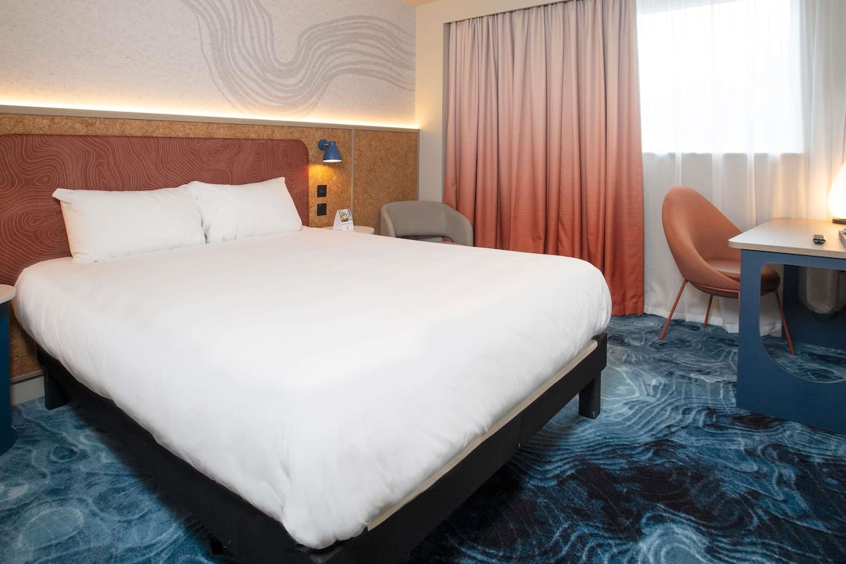Habitación de hotel con una cama grande, un escritorio, una silla y vistas al exterior.