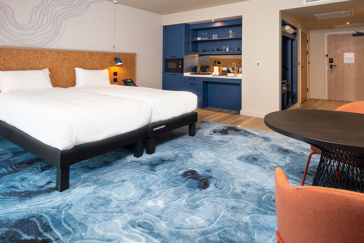 Habitación de hotel con cama, escritorio, silla y kitchenette.