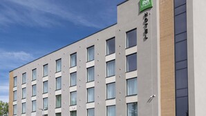 Ein modernes Hotelgebäude mit einer flachen Fassade, zahlreichen Fenstern und einem grünen Schild, das es als ibis Hotel kennzeichnet.