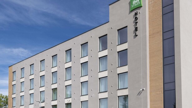 Un moderno edificio de hotel con fachada plana, múltiples ventanas y un letrero verde que indica que es un hotel ibis.