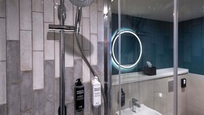 A modern bathroom with a glass-enclosed shower, a white sink, and a mirror with a circular light. - ibis Styles Burton Upon Trent - Hotel & Suites (Burton on Trent)